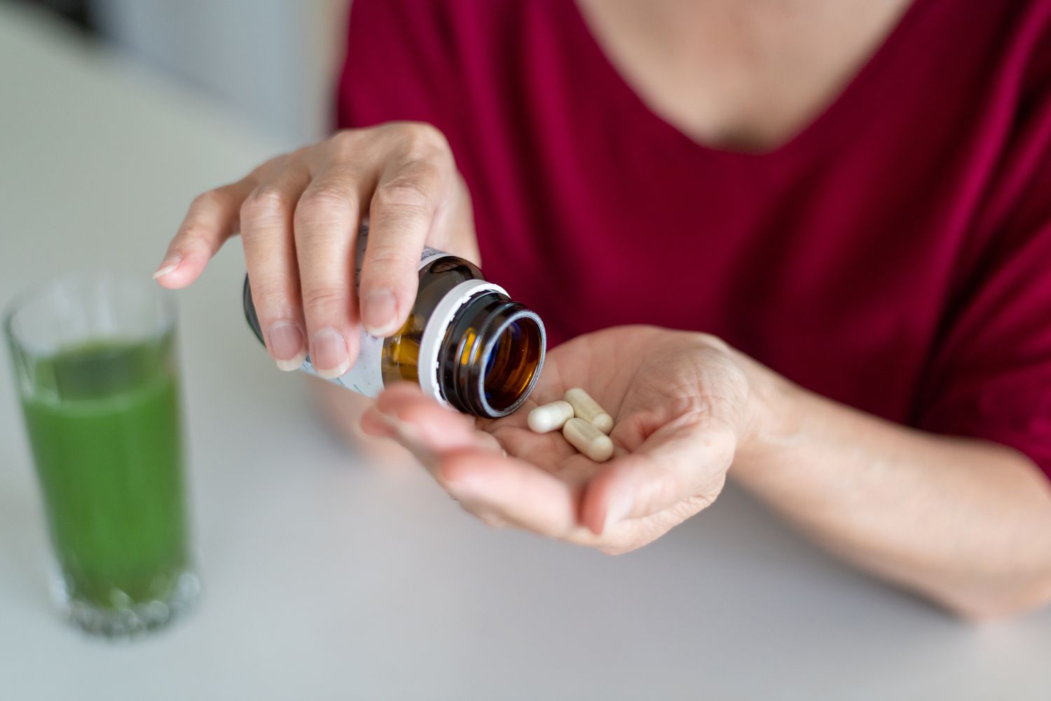 A woman taking daily capsules with a healthy green smoothie in the background.