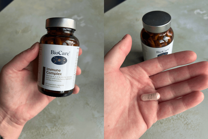 A close-up view of an adult hand holding small capsules of BioCare Immune Complex.