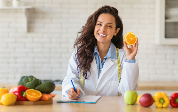 A professional dietitian or health coach standing next to a variety of healthy food options.