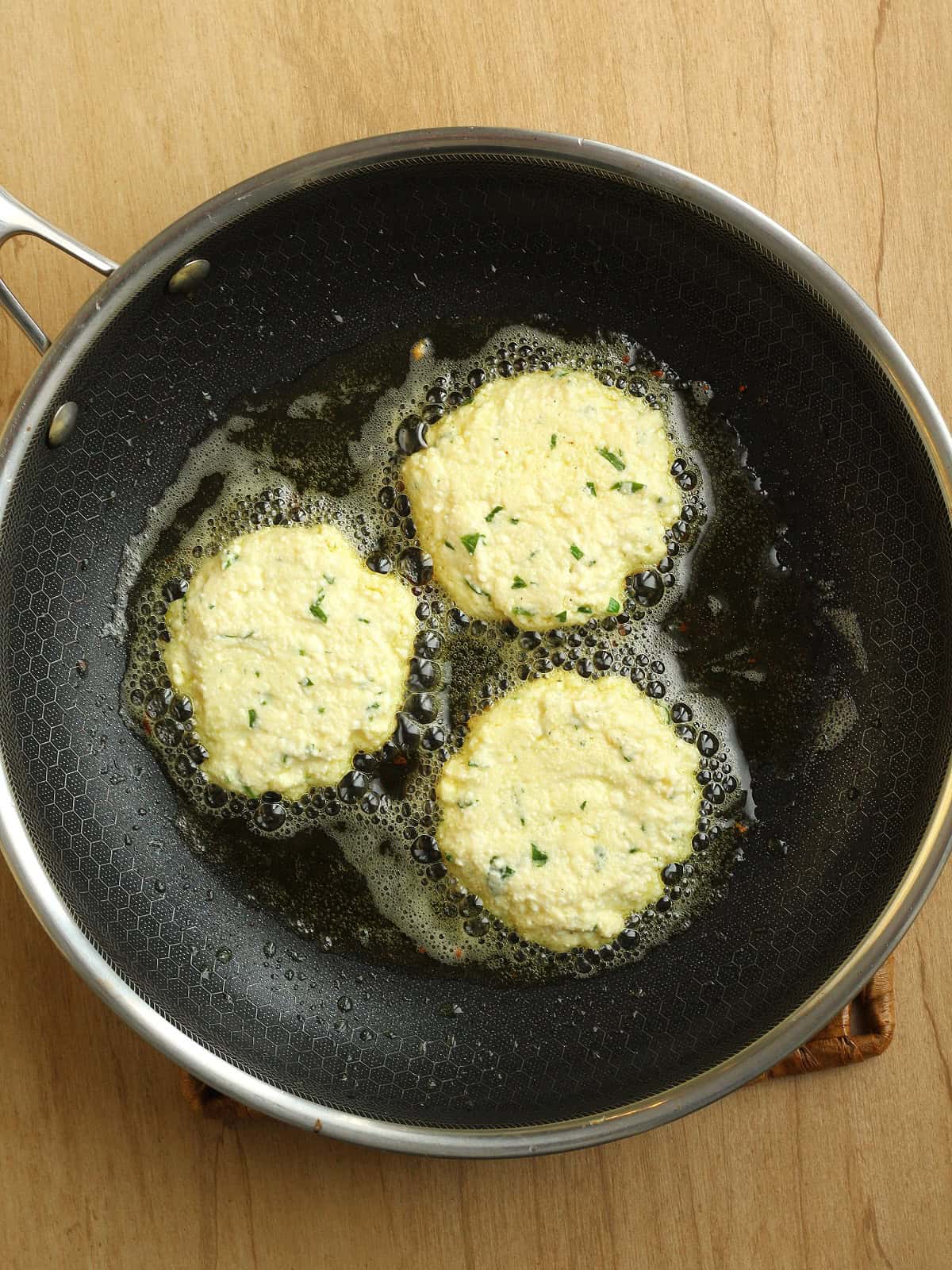 Ricotta fritters being pan-fried in a shallow layer of olive oil in a non-stick skillet.