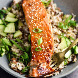 A close-up shot of a silver fork flaking a piece of glazed, cooked salmon.