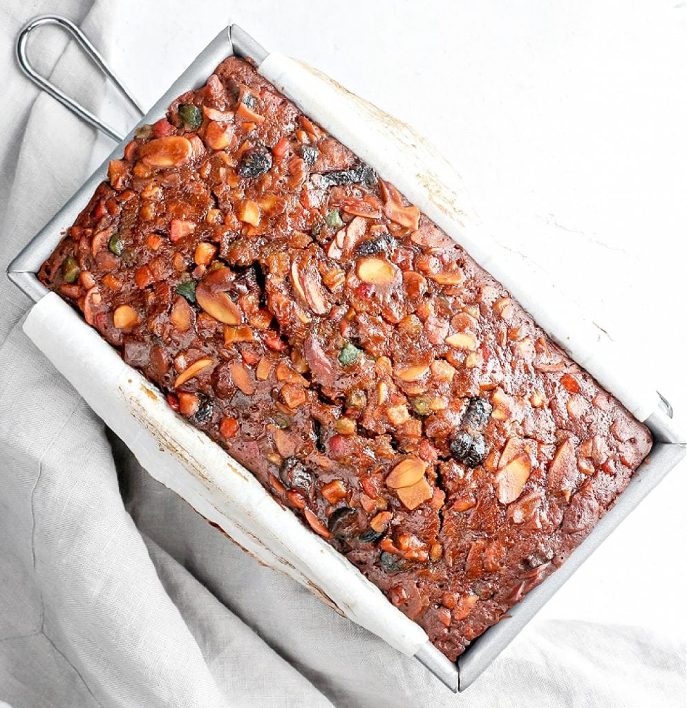 A close-up slice of moist vegan Christmas fruitcake showing candied fruit and nuts.