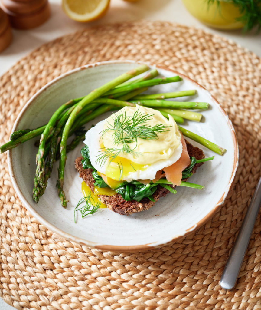 A serving of Eggs Royale presented on toasted rye bread with a side of fresh greens.