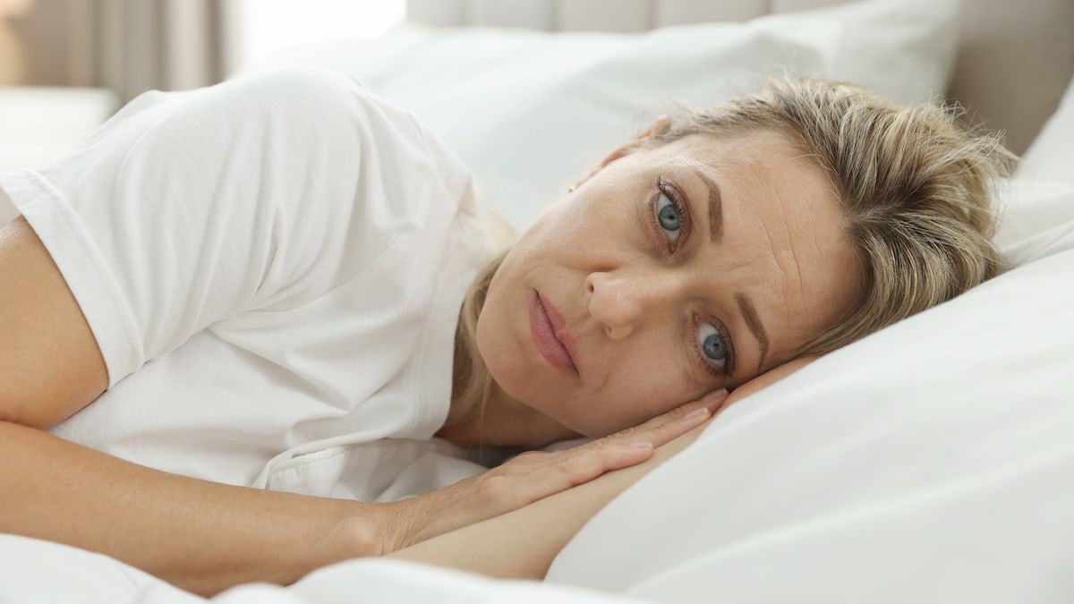 A woman lying awake in bed looking distressed, representing the struggle with irregular sleep patterns.
