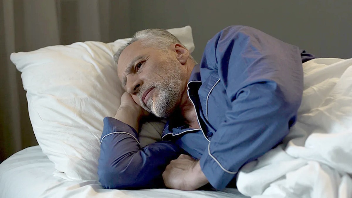 A man lying in bed looking awake and focused, representing a disciplined sleep-wake routine.
