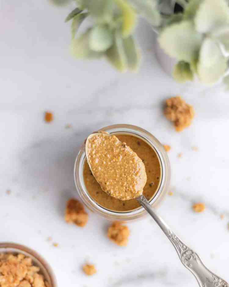 A spoon lifting a thick, smooth swirl of granola butter out of a mason jar.