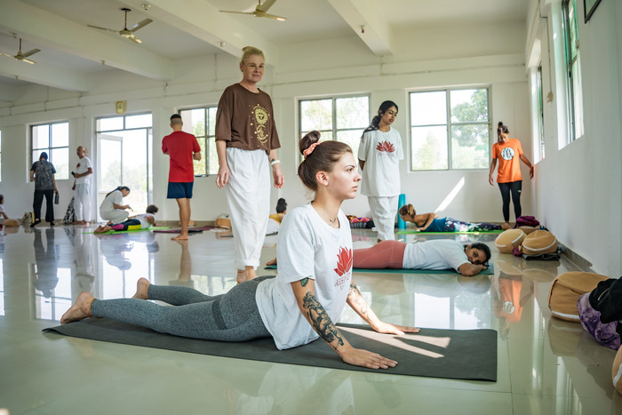 A yoga instructor providing manual alignment adjustments to a student in Cobra Pose.