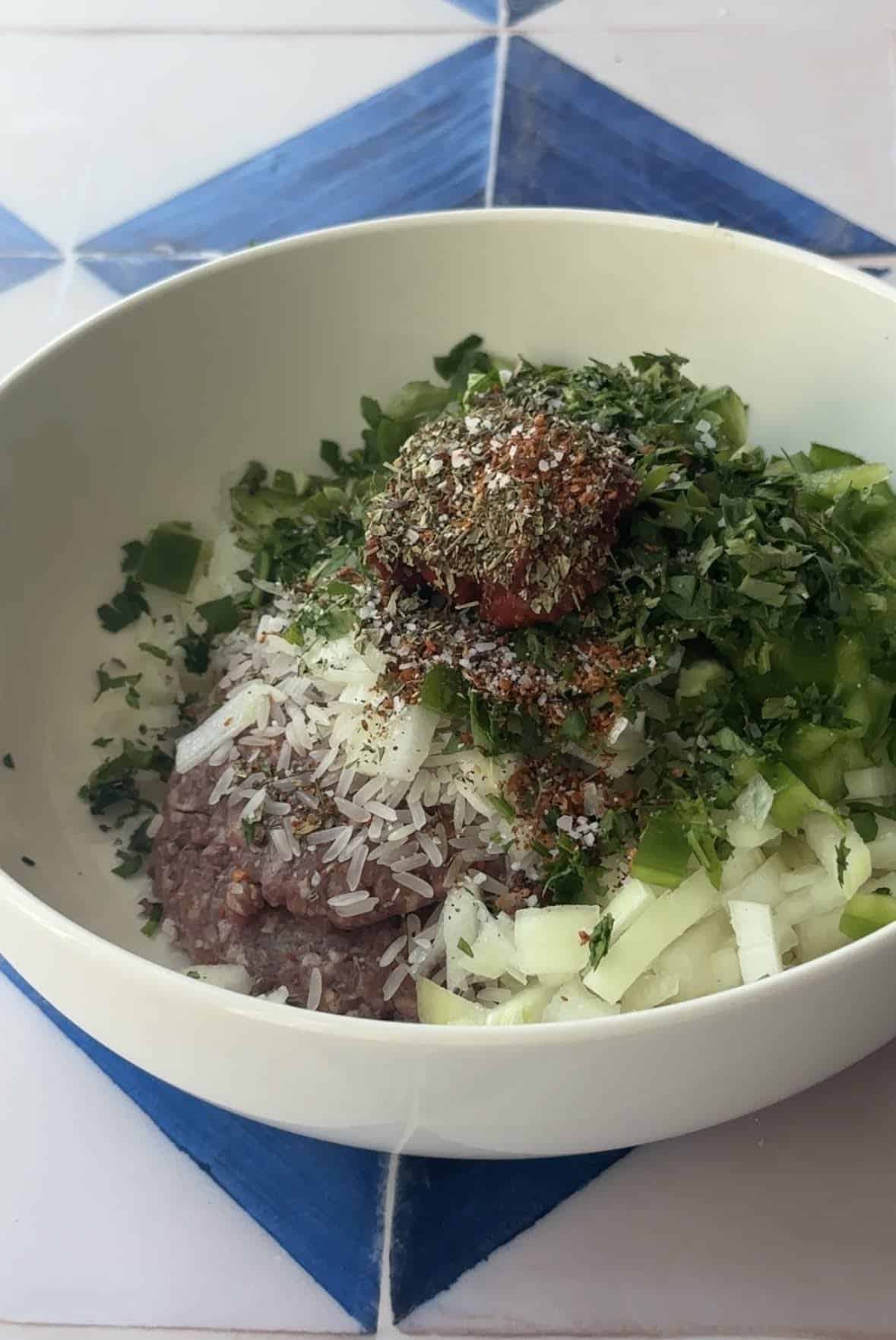 A bowl containing raw ground meat, rice, and fresh herbs ready for mixing.