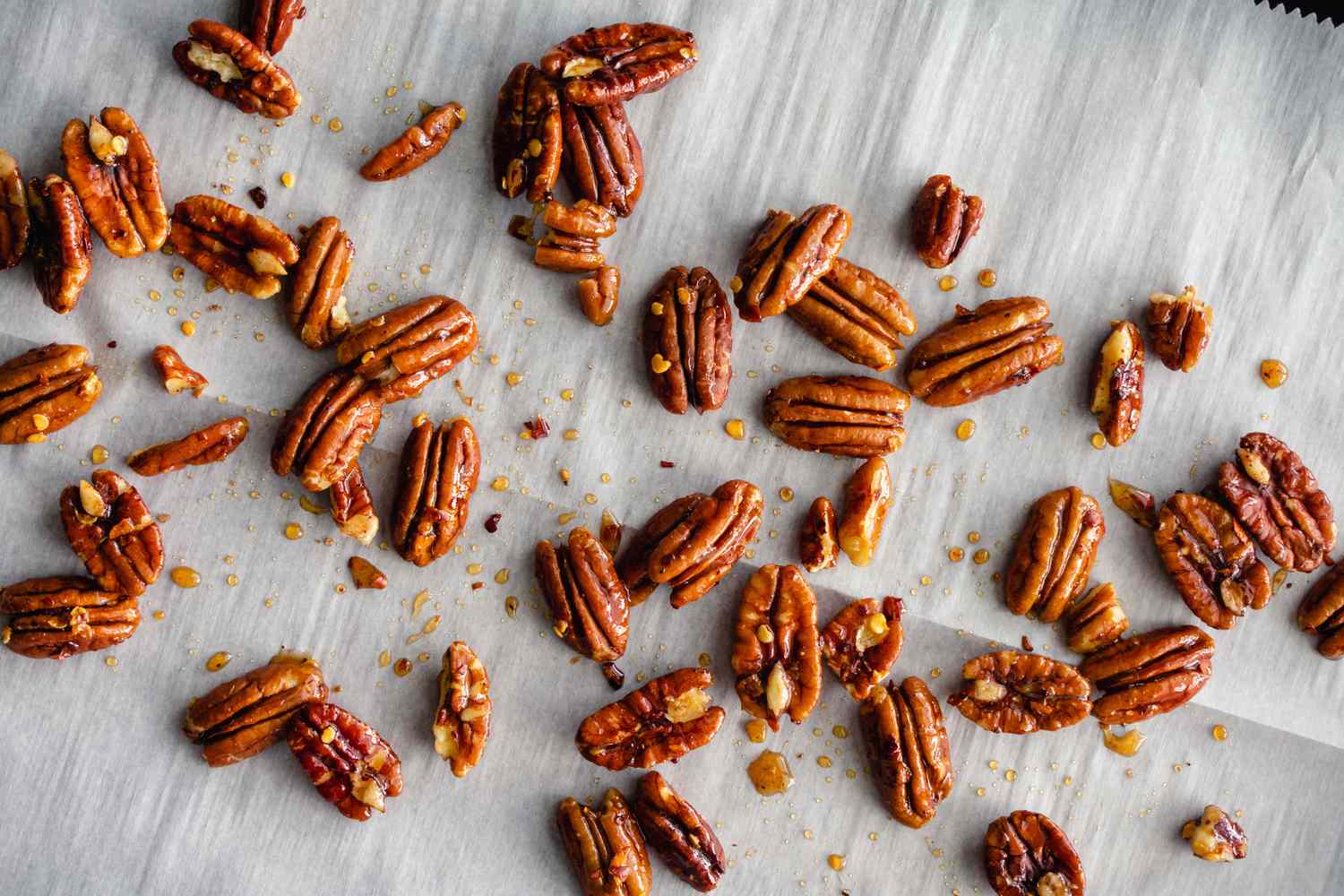 Whole pecan halves scattered naturally on a piece of parchment paper.