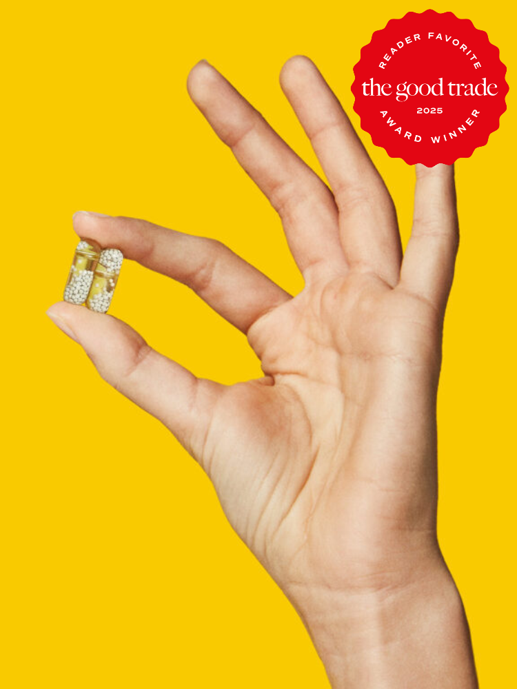 A hand holding two clear Ritual vitamin capsules against a bright yellow background.