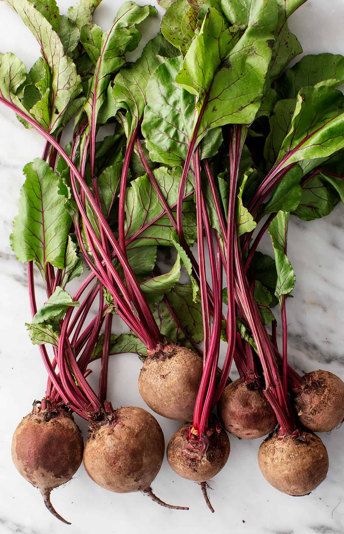 A bunch of fresh red beets with vibrant green leaves still attached on a neutral background.
