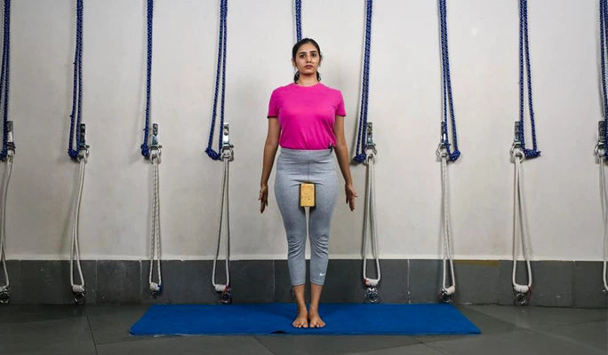 A practitioner in Mountain Pose (Tadasana) holding a wooden block between their thighs for alignment.