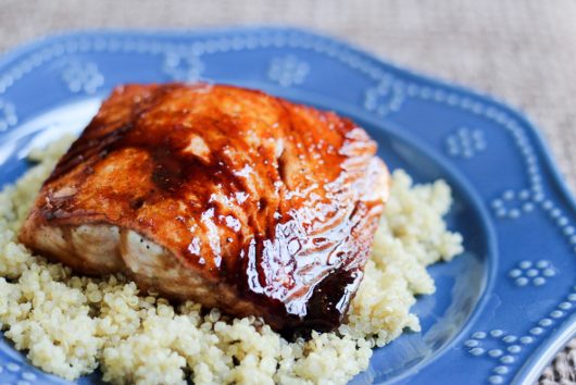 Carefully placing a glazed salmon fillet on top of a portion of black rice.
