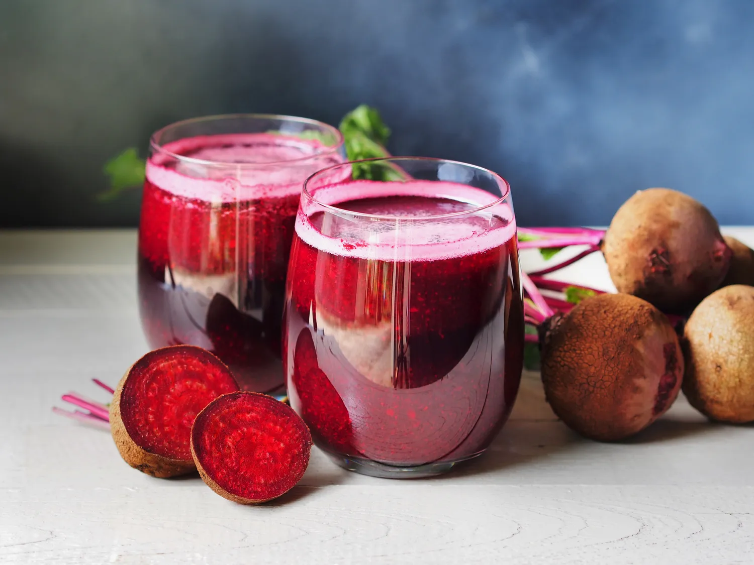 A glass of dark red beet juice on a wooden table next to fresh beetroots.