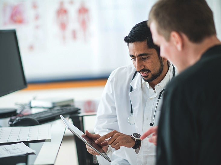 A healthcare professional in a white coat talking to a patient in a clinical setting.