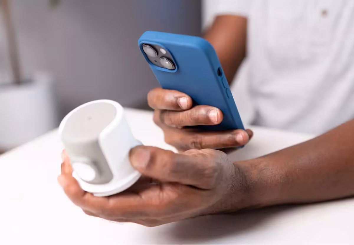 A person holding a CGM sensor in one hand and a mobile phone displaying a live glucose line graph in the other.
