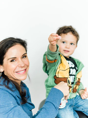 A child sitting with their parent holding a bottle of Raise Them Well vitamins.