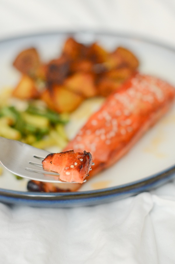Salmon fillet soaking in a dark honey tamari marinade in a glass bowl.