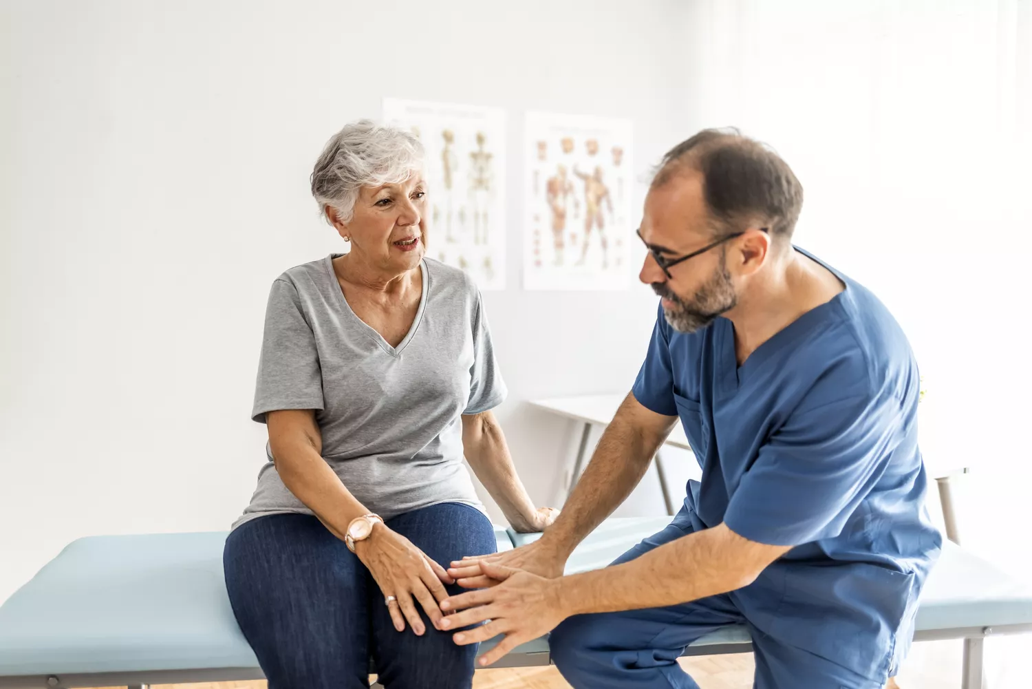 A senior woman in a clinic discussing her condition with a healthcare provider who is offering supportive care.