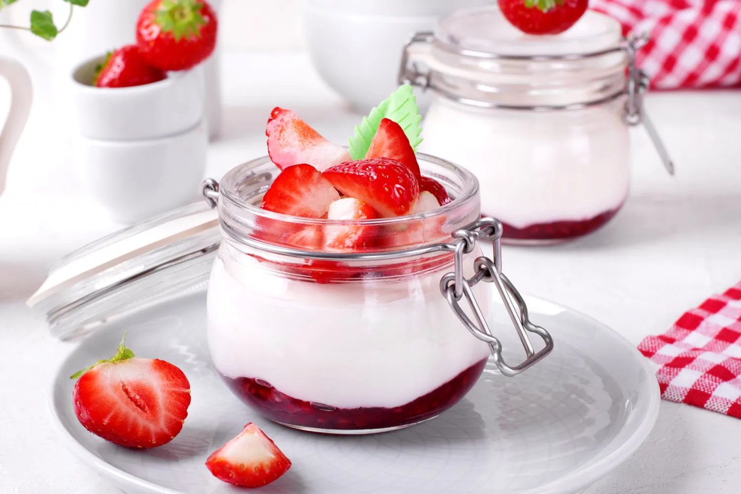 A glass jar of yogurt topped with a fresh strawberry.