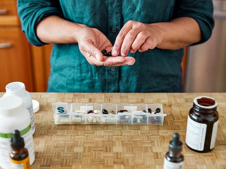 Top-down view of a person sorting various supplement capsules into a wooden weekly pill organizer.
