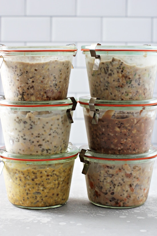 Six prepared mason jars filled with oatmeal and fruit stacked together for weekly meal prep.