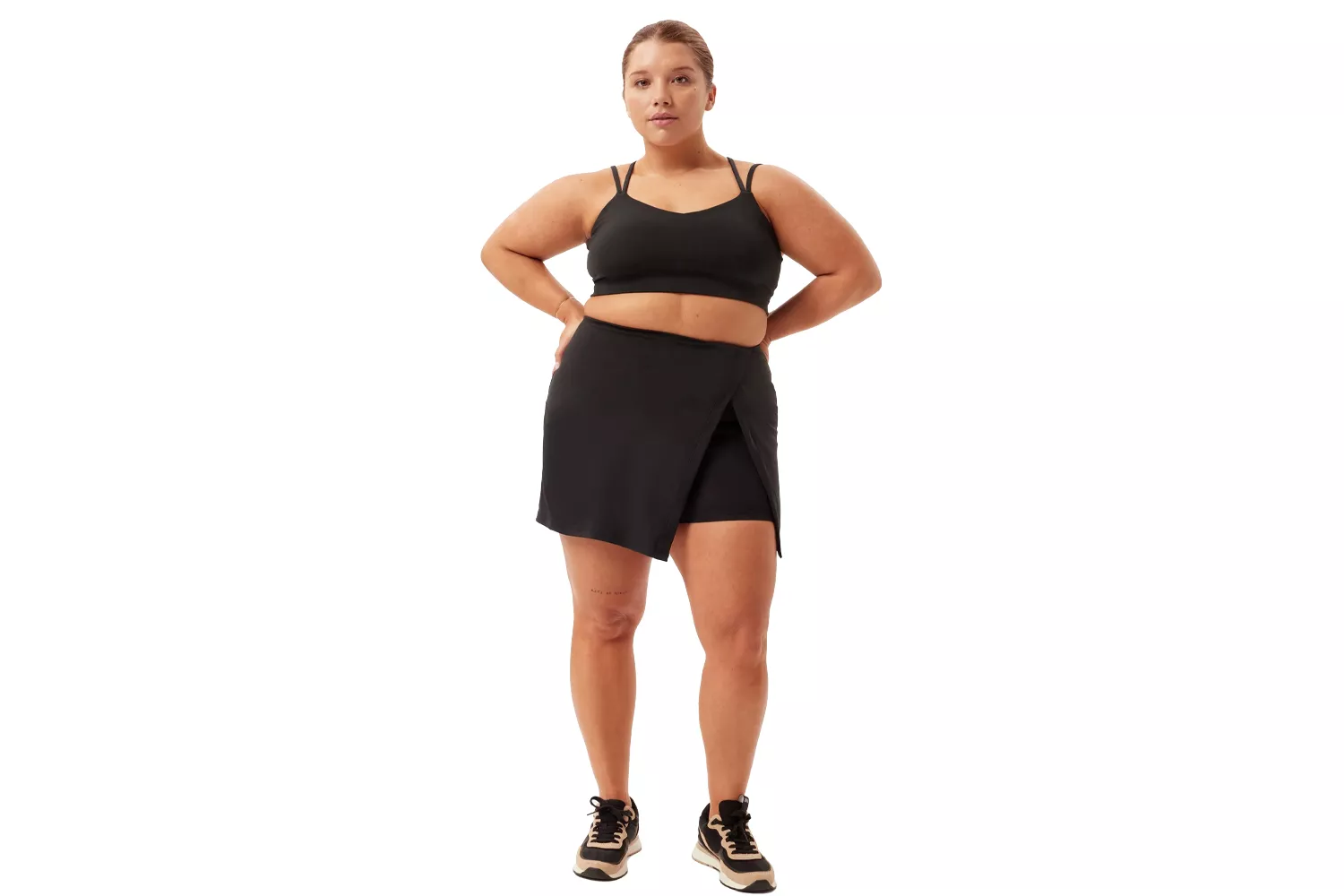 A woman in a black athletic skort and sports bra posing confidently against a white background.