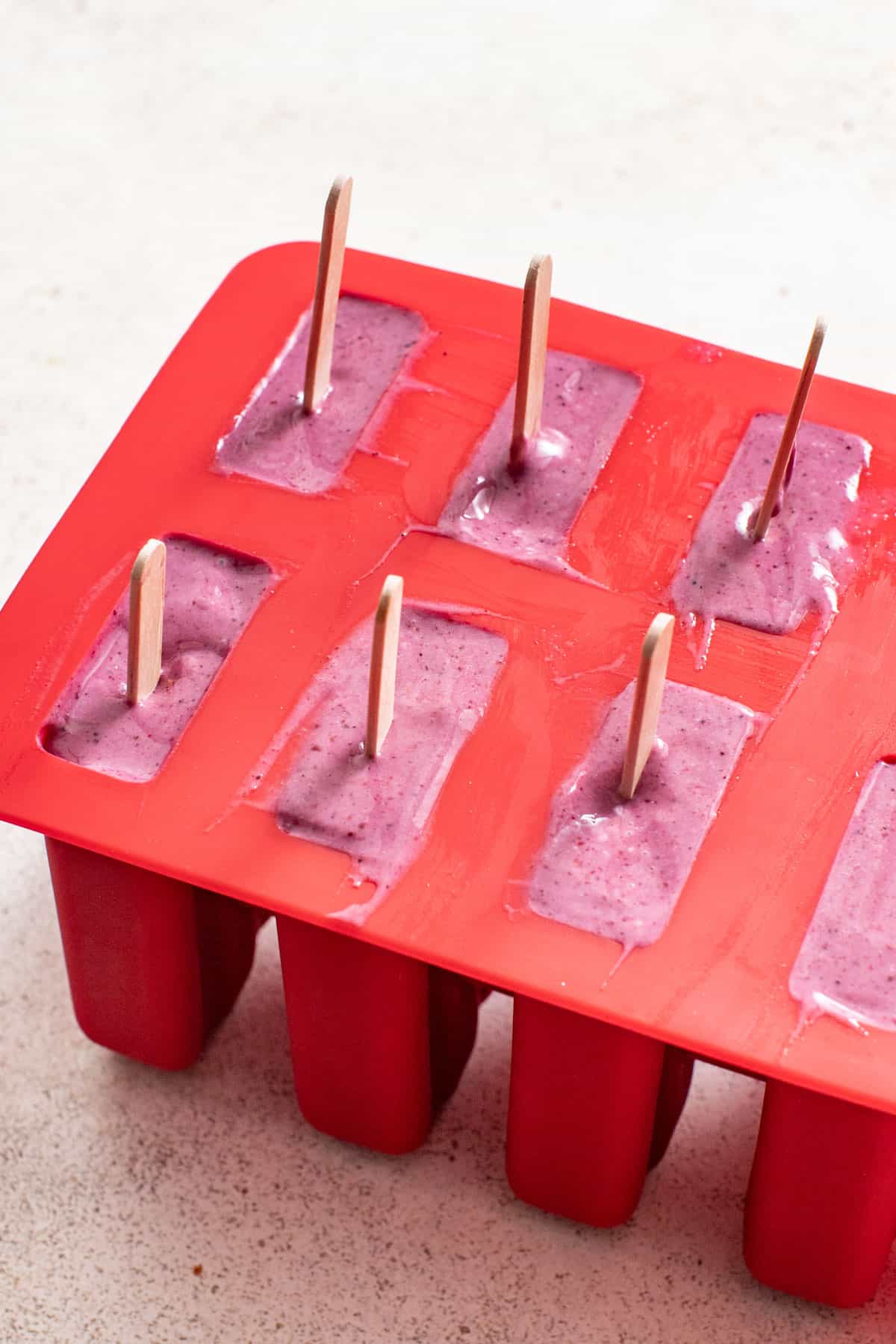Frozen berry popsicles with wooden sticks still in their silicone molds.