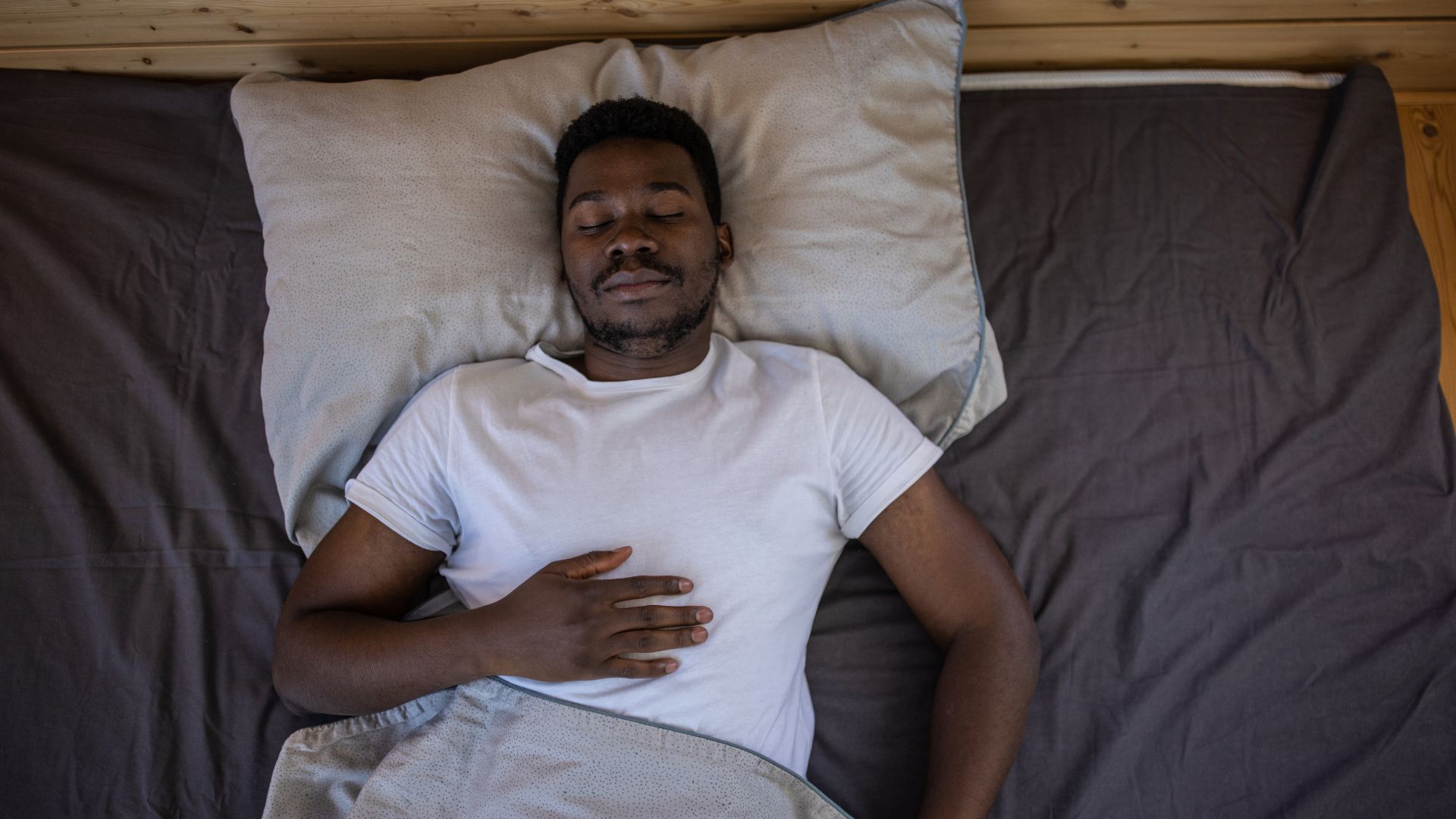 A man resting deeply in a comfortable bed with his eyes closed.