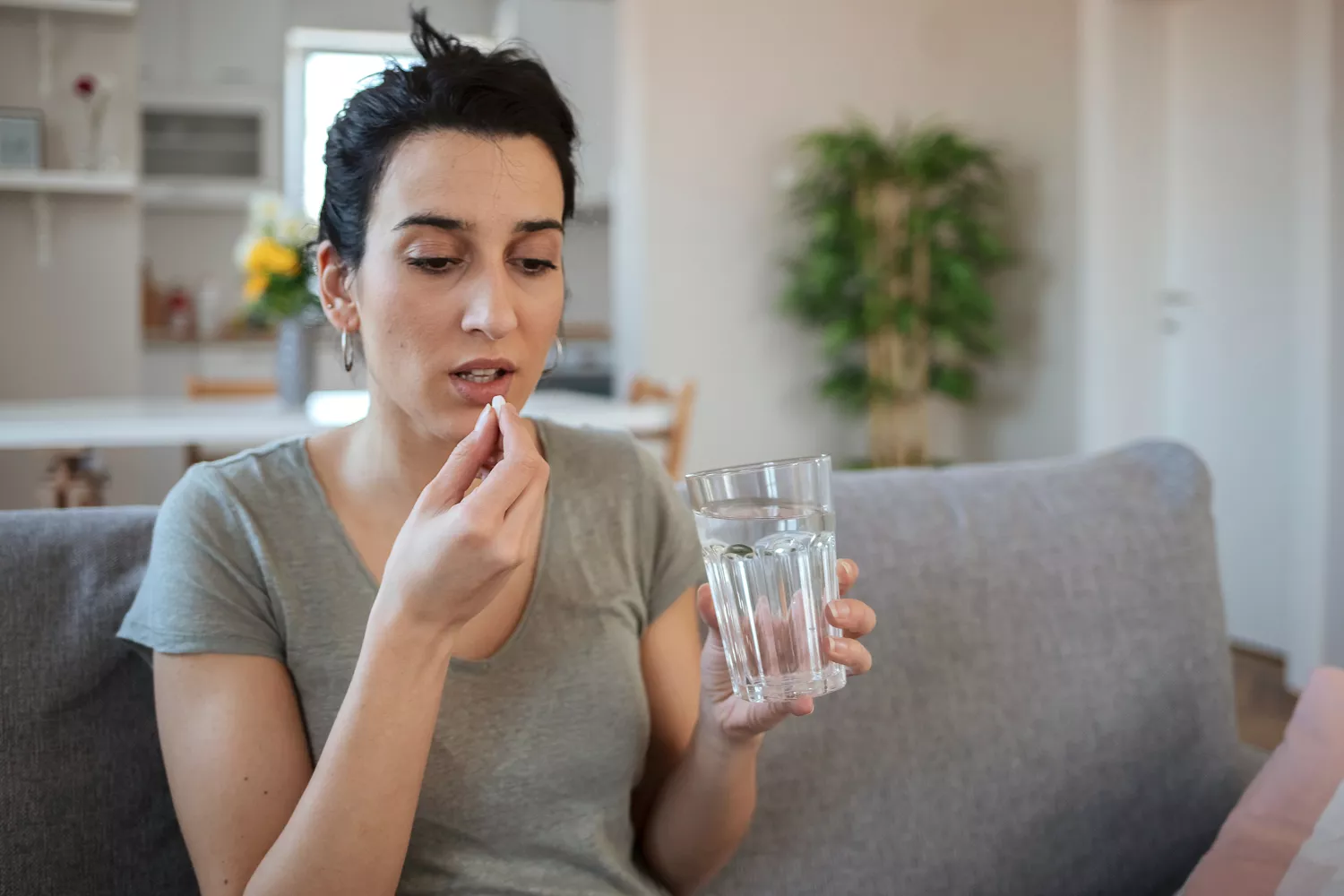 A woman holding a glass of water and preparing to take a metronidazole tablet.