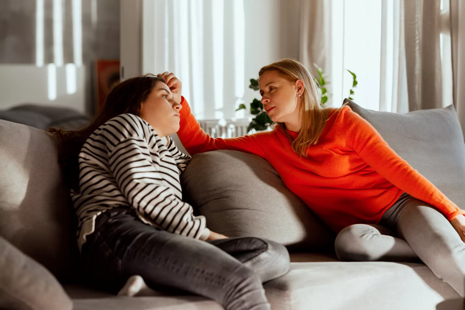 An adult comforting a young person on a sofa at home.