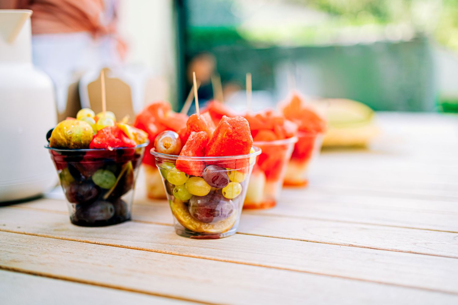 Small cups filled with various cut fruit pieces on a wooden table.