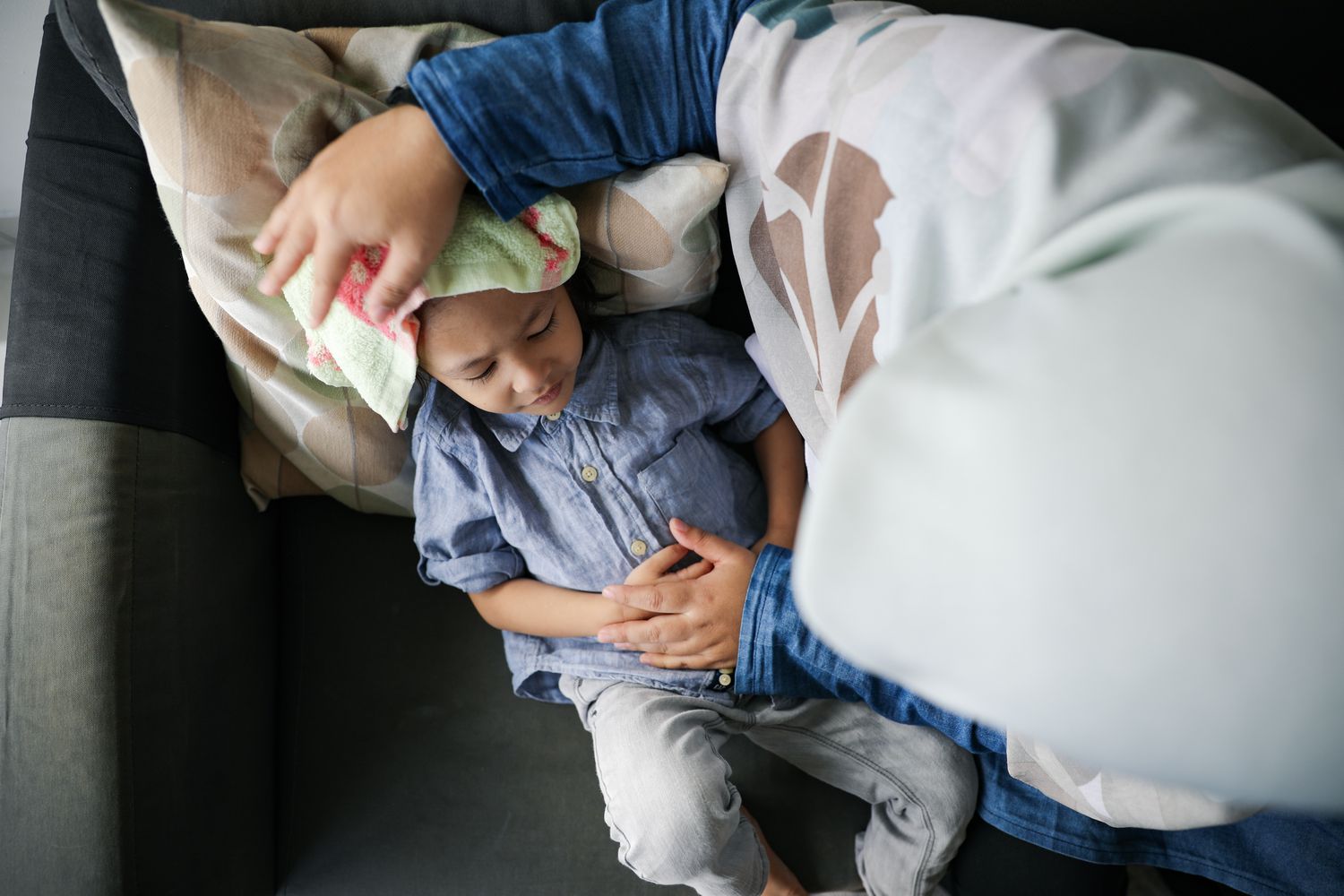 A caregiver's hand gently comforting a sick child at home.
