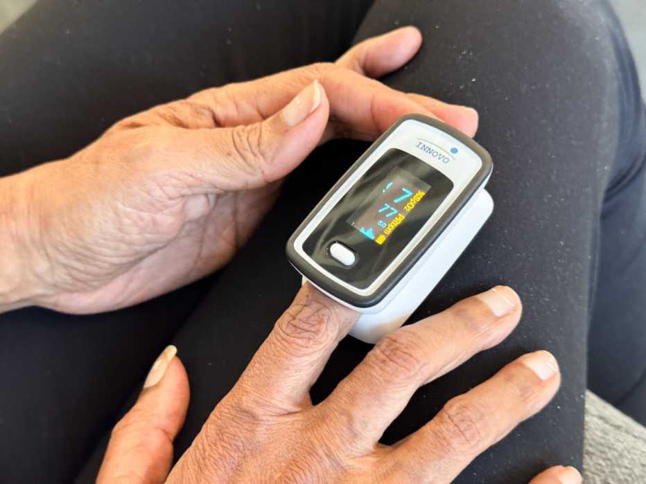 A close-up shot of a user's finger inserted into a pulse oximeter during a health check.