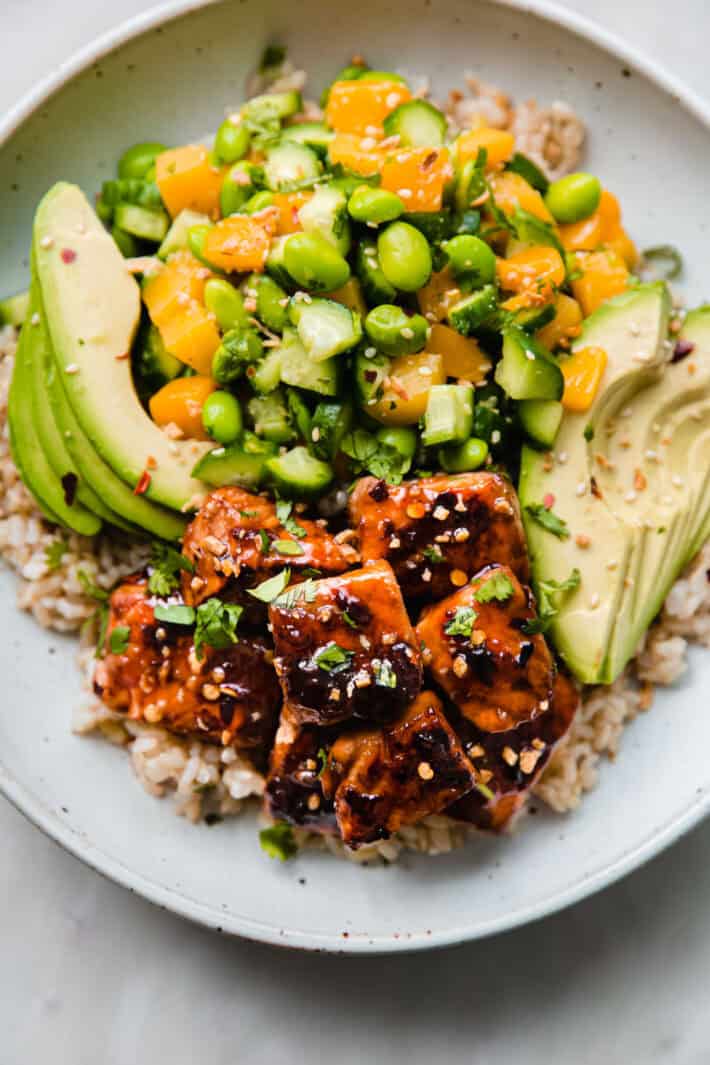 Two completed rice bowls topped with glazed salmon pieces, sliced avocado, and fresh herbs.