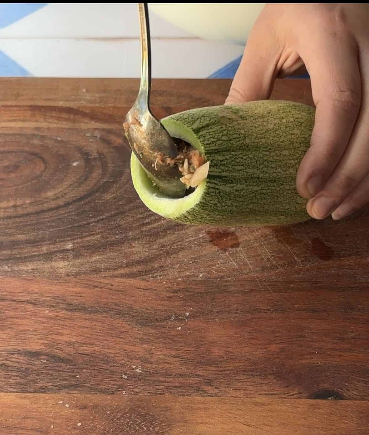 A hand filling a hollowed vegetable with a rice and meat mixture.