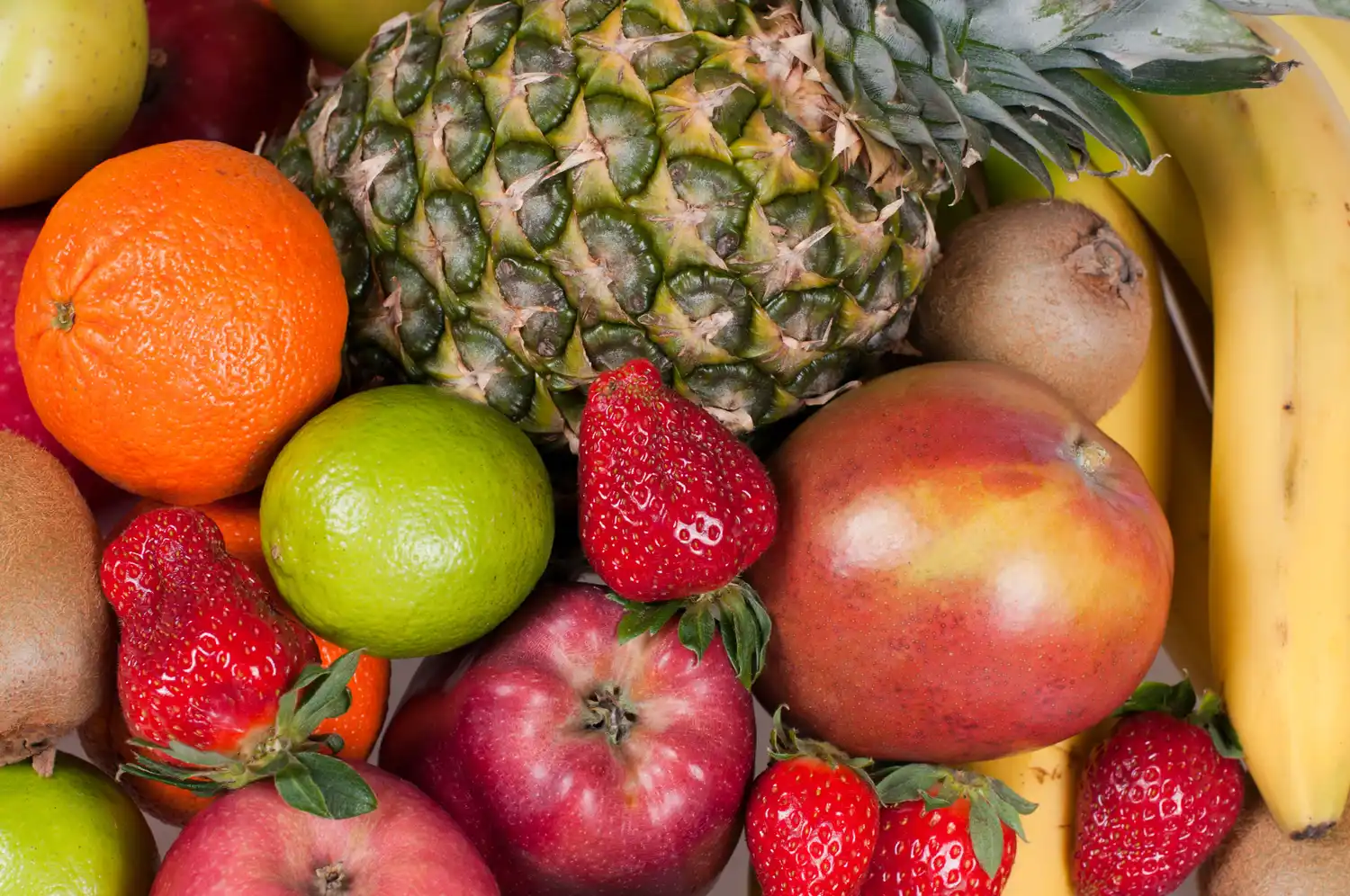 A vibrant assortment of whole fruits including pineapples, strawberries, and kiwis.