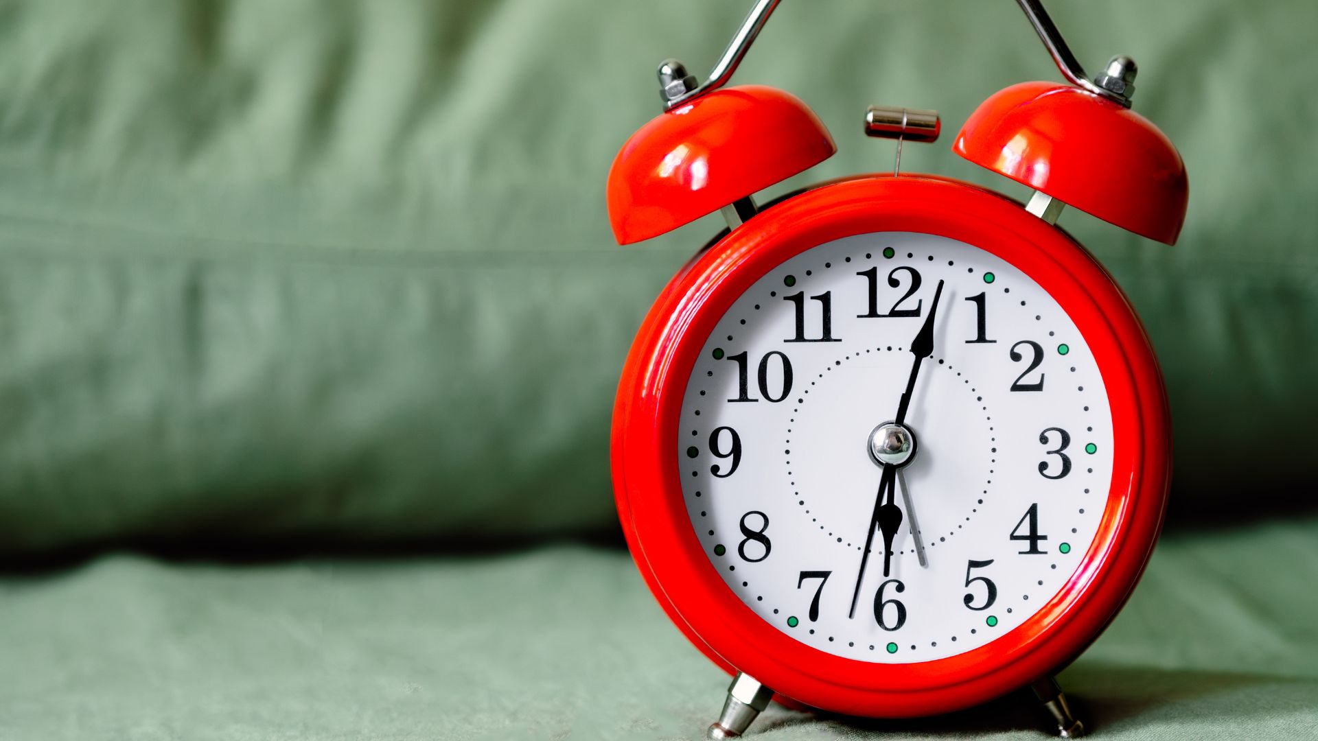A classic red alarm clock resting on a white bedsheet.