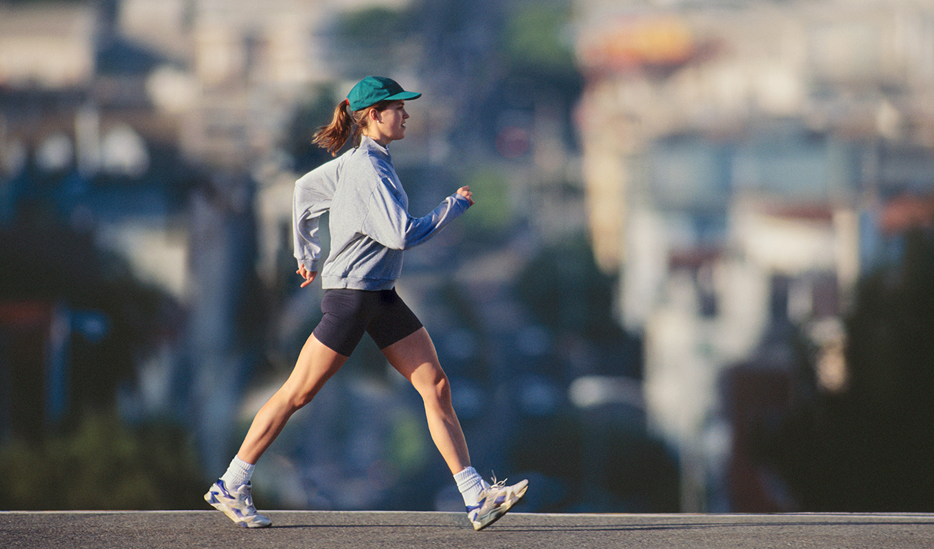A runner transitioning from a walking pace to a light jog on a paved outdoor path.