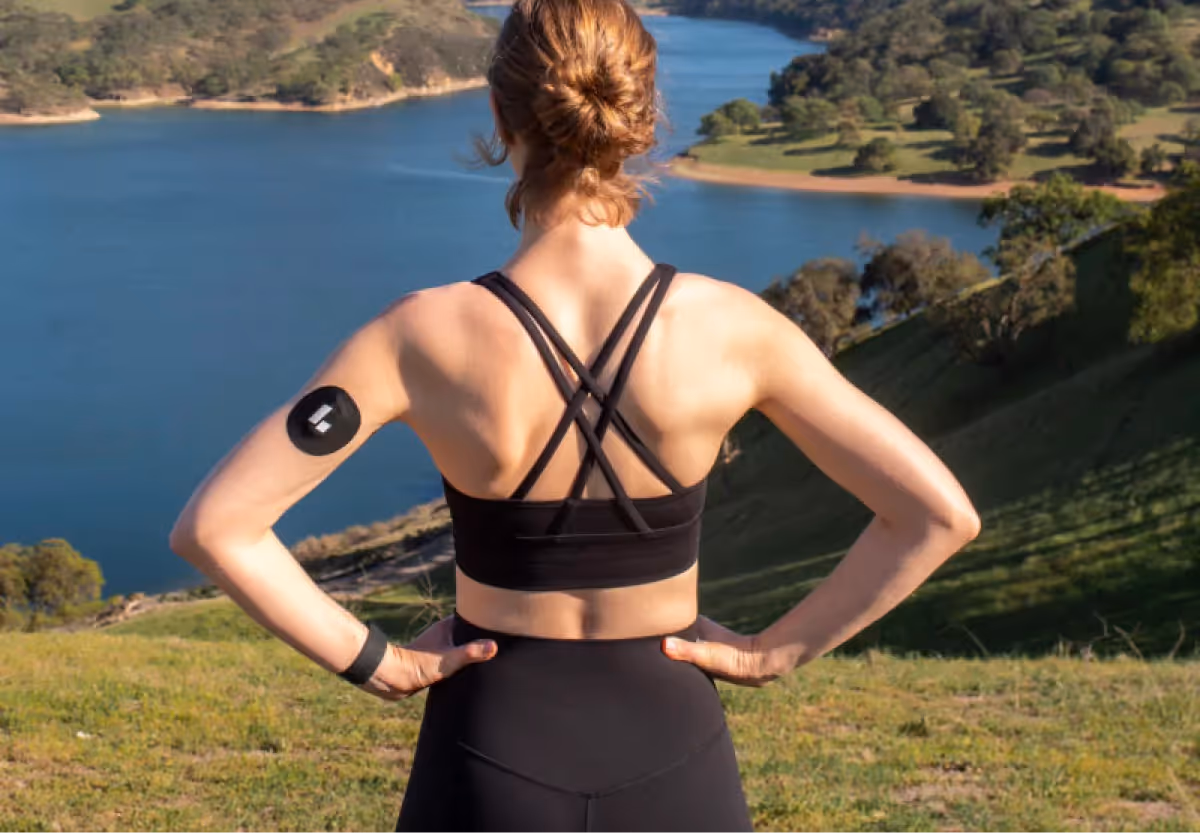 A woman wearing a Levels-branded CGM sensor on her arm while smiling.
