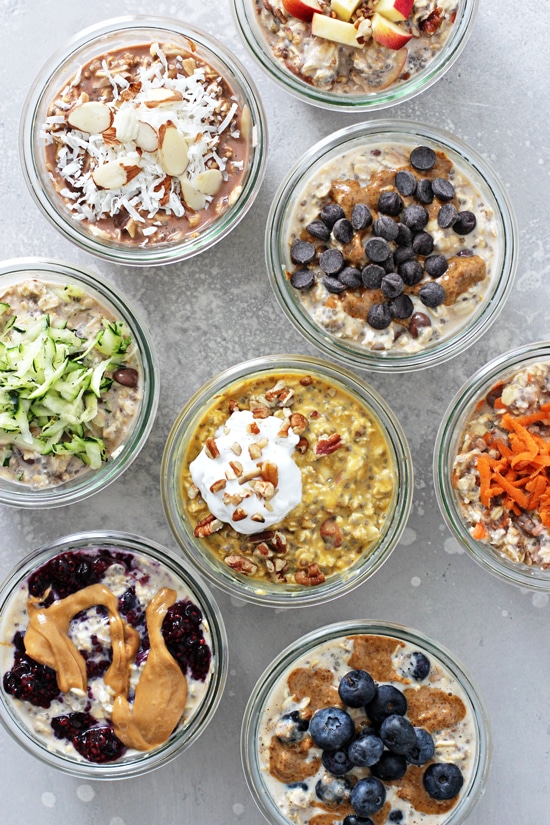 Eight small glass jars arranged in rows, each containing a different colorful flavor of vegan overnight oats.