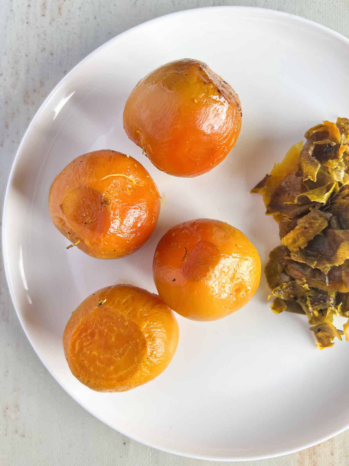 Whole roasted golden beets on a white plate with the skins removed and sitting to the side.