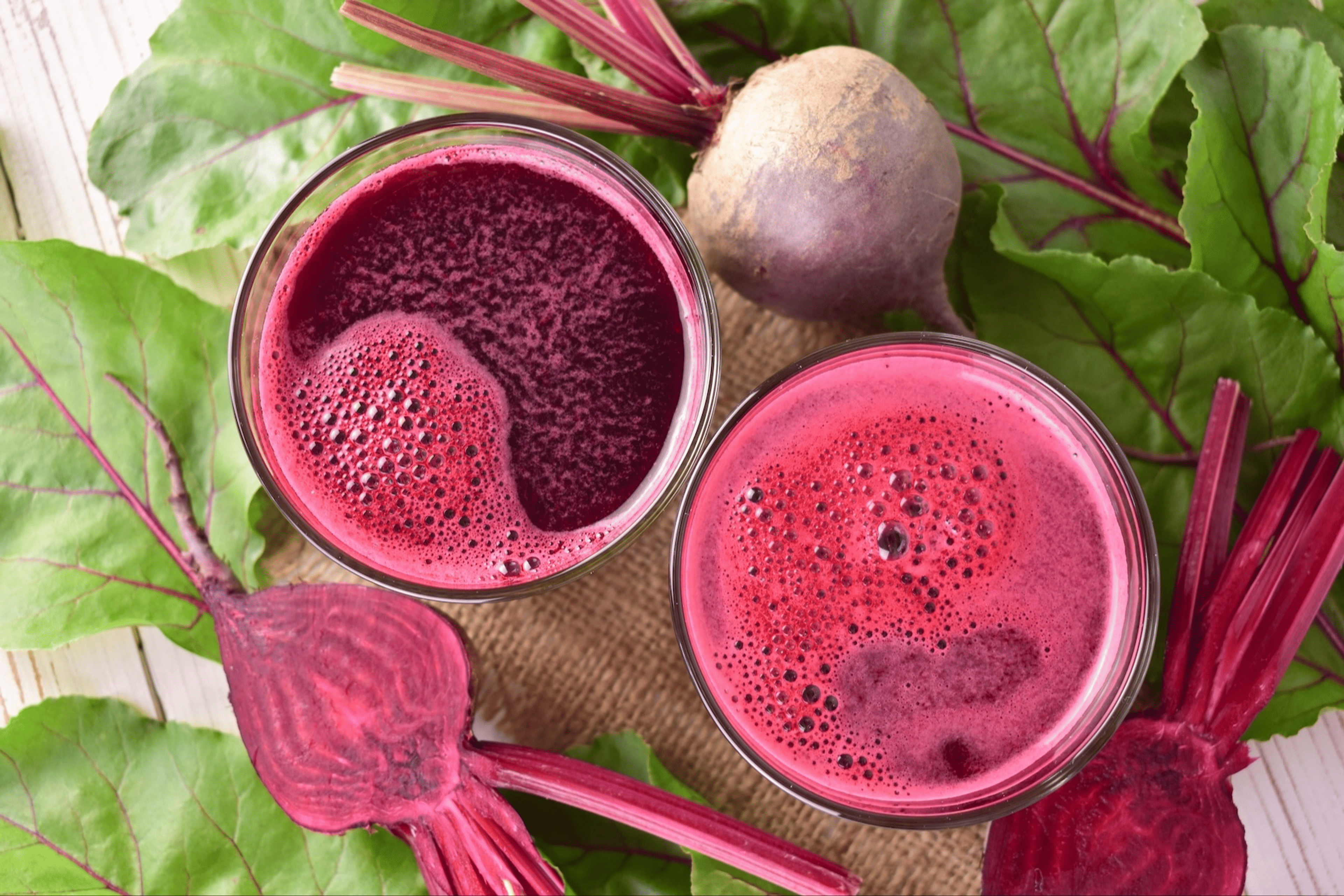 Bird's-eye view of beet juice glasses surrounded by whole raw beetroots.