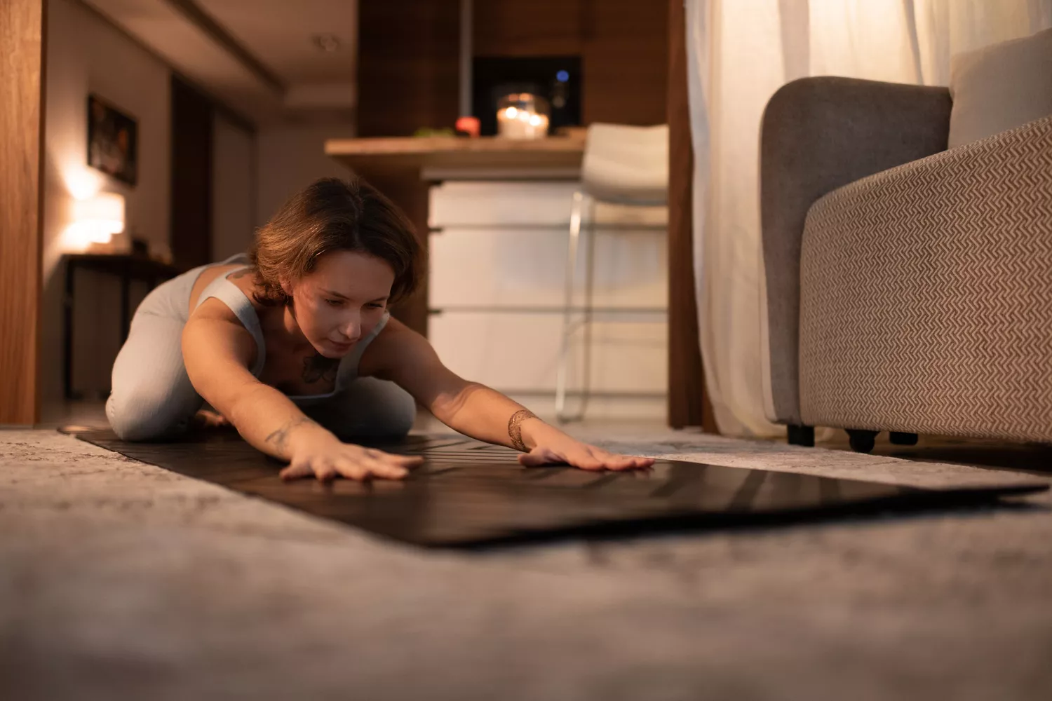 A woman practicing yoga stretches on the floor in a dark room at night.
