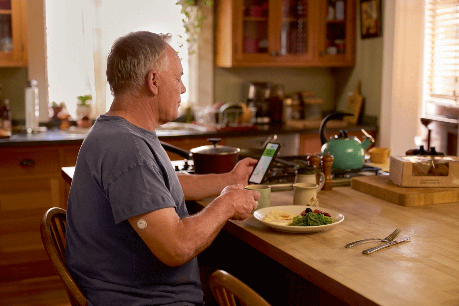 A FreeStyle Libre 3 Plus sensor on an arm next to a breakfast plate and smartphone.