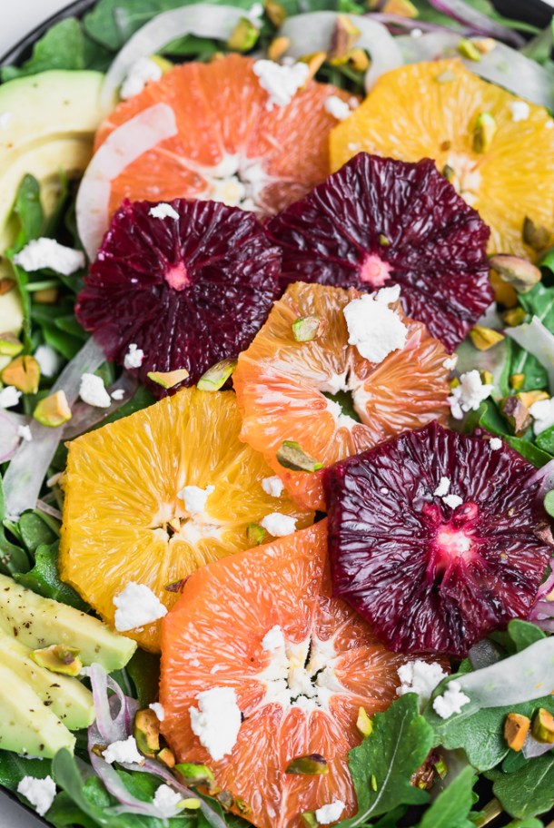 Close-up of salad dressing being poured over fresh greens and citrus.