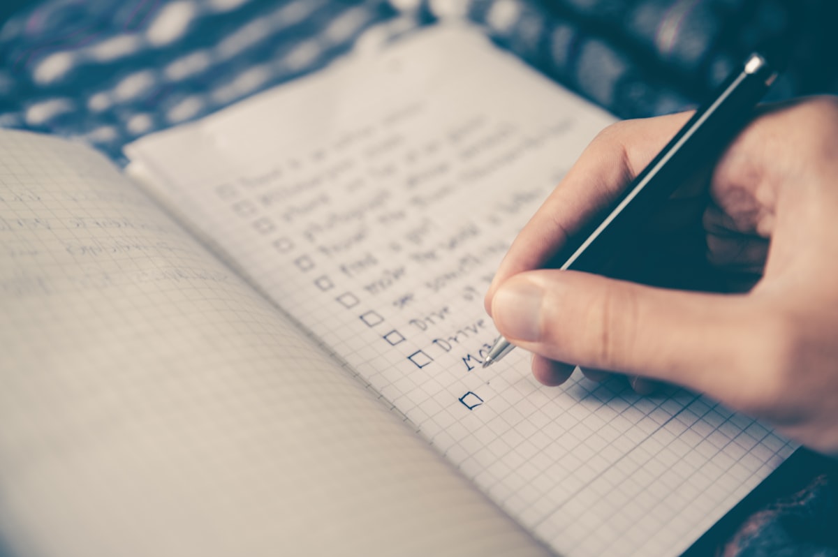 A hand writing a detailed list in a planner to organize daily tasks.