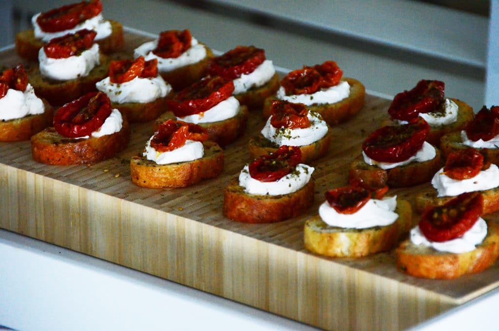 Artistically arranged labneh crostini on a wooden board topped with roasted tomatoes and za'atar.
