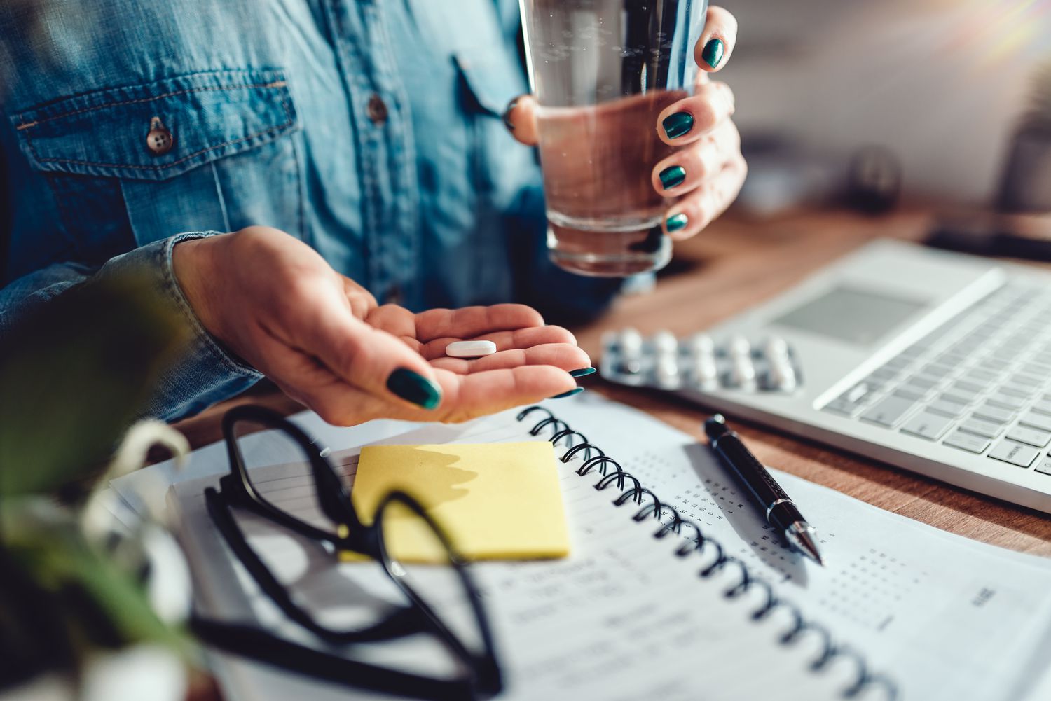 A person holding a pill and a glass of water at a desk, representing health management and medication.