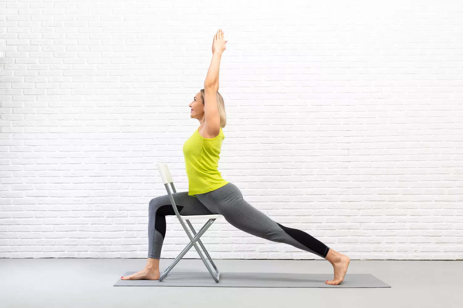 A practitioner performing a supported high lunge using a chair for balance.